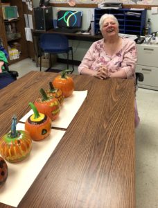 A woman served in CLI's ROW program smiles in front of a long line of decorated pumpkins.